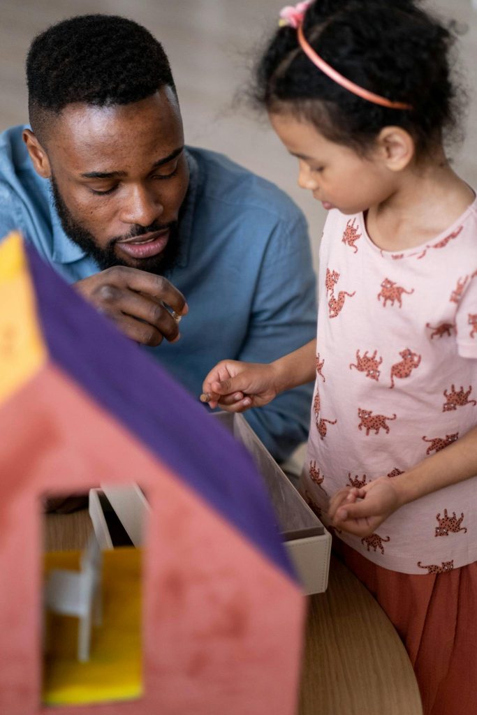 A father and daughter enjoying quality time together playing with a dollhouse indoors.